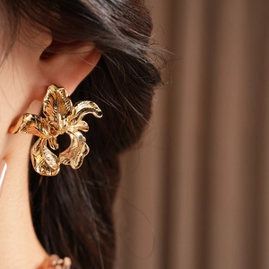 Close-up of golden irregular flower earring worn on ear with elegant metallic texture