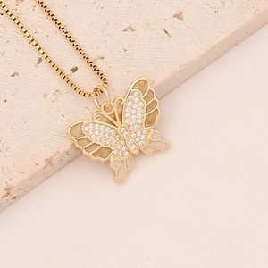 Close-up of gold butterfly pendant with zircon crystals on beige stone background