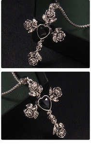 Detail of silver cross necklace with black heart gemstone and rose floral accents