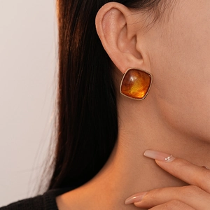 Close-up of amber resin square stud earrings with gold trim worn by a model