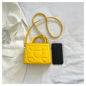 Mini sac bandoulière jaune avec motifs cœurs en relief, comparé à un smartphone pour la taille