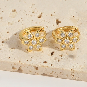 Makroaufnahme goldener Blumenohrringe mit klarem Zirkon auf beigem Stein hintergrund