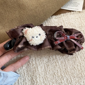 Détail d'une pince à cheveux avec ours en peluche et nœud à carreaux en tissu brun