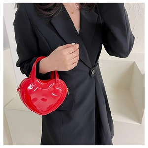 Detail of a shiny red heart-shaped patent leather handbag held by a model in black