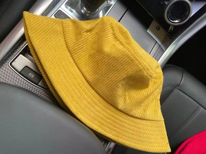Detail view of a yellow corduroy bucket hat placed on a car dashboard in natural light