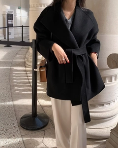 Detail of a black wool coat featuring a large lapel and waist belt in a classic gallery