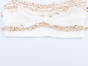 Detail of bohemian white crop top with woven trim and bead charms on textured fabric