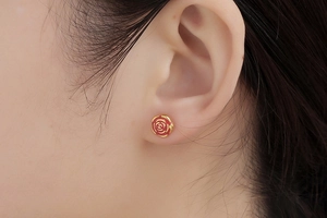 Detailed close-up of a gold-plated rose-shaped earring with elegant red enamel finish