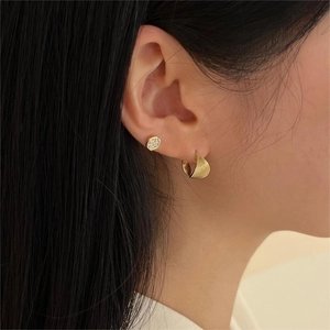 Close-up of elegant gold twisted hoop earring and textured stud worn by a model