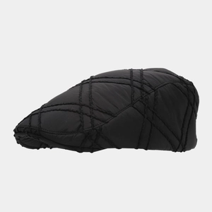 Detail of black quilted newsboy cap showing geometric stitching and warm texture