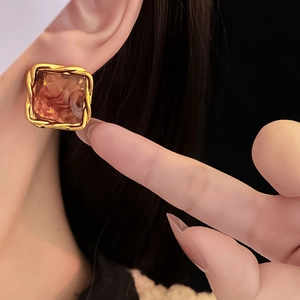Detail of amber geometric resin earrings with twisted gold frame worn by a model