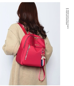 Detail of red water-resistant oxford backpack featuring golden hardware and a cute toy bear charm