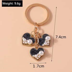 Detail of gold keychain with black heart charms and inlaid pearls on a pink background