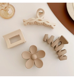 Set of four matte milk tea hair claws in floral and geometric shapes on a minimalist desk