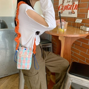 Checkered crossbody bag with orange ruffle strap shown in a cozy cafe setting