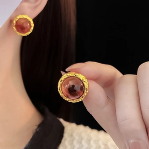 Detail of round gold-textured earrings with red-brown resin gems on a model