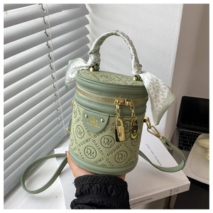 Detail view of a green cylinder bag with DM embossed pattern and decorative silk scarf handle