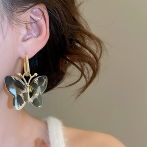 Close-up detail of leopard print acetate butterfly earring on model in warm studio lighting