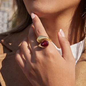Nahaufnahme eines goldenen Doppel-Tropfenrings mit rotem Edelstein am Finger