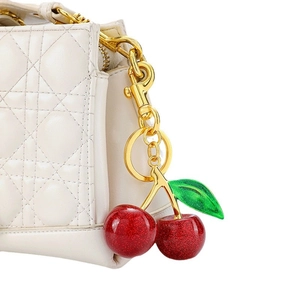 Sparkly red cherry bag charm with green leaf and gold hardware on white quilted bag