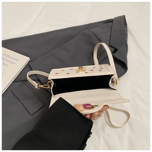 Detail of a creamy white crossbody bag with cherry prints and golden hardware buckles
