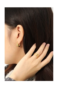 Detail of minimalist gold U-shape hoop earrings and wavy ring on a model