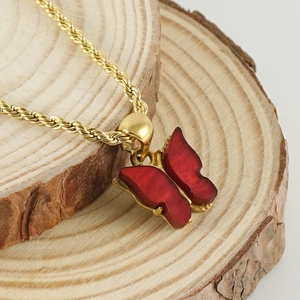 Golden twist chain necklace with a red matte butterfly pendant on a natural wood surface