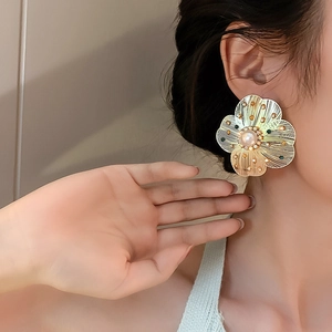 Detail of a large gold hollowed flower earring with a pearl center on model
