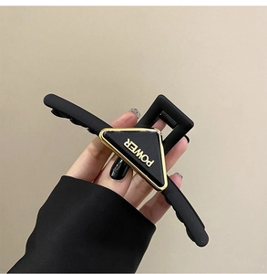 Detail of matte black shark hair clip with golden POWER lettering on triangle leather