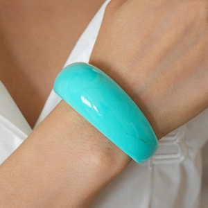Close-up of vibrant cyan resin bangle featuring a glossy mirror finish on a model's wrist