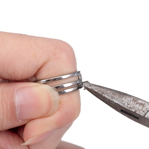 Triple layer stainless steel open ring in silver finish held by pliers for durability test