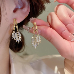 Close-up of elegant gold leaf earrings with inlaid clear zircons worn by a model