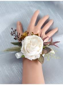 Detailed wrist corsage featuring a white silk flower, berries, and green foliage with ribbon