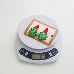 Detail shot of embroidered green Christmas tree hair clips weighing 6.5g on a scale