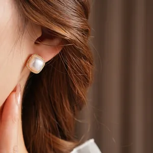 Square gold-plated stud earrings with pavé zircons and white pearl center on model