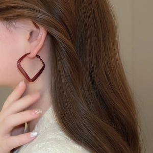 Detail of dark red geometric rhombus earrings with glossy finish on a model