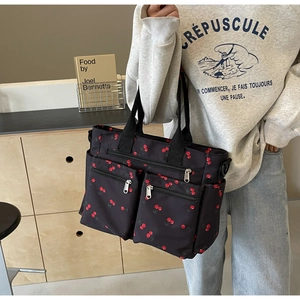 Detail of black nylon tote bag with cherry print and multi-pocket design on model
