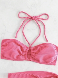 Flat lay of bright pink halter bikini top featuring ribbed texture on marble surface