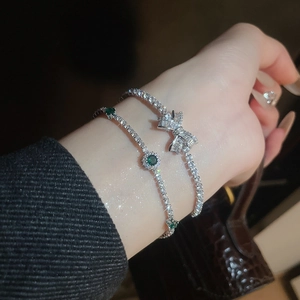 Close-up of sparkling bow-knot tennis bracelet with green gemstone detail on wrist