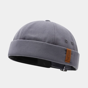 Detail of gray canvas docker hat featuring a leather logo patch and adjustable metal buckle