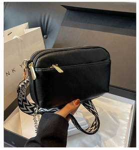 Detail of black PU crossbody bag featuring gold zipper and geometric strap on gift box