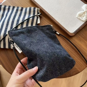 Detail of striped canvas crossbody bag with simple wish label on a wooden desk