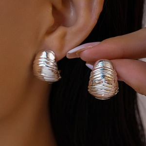 Détail de boucles d'oreilles argentées en acrylique avec texture plissée portées par modèle