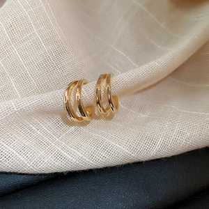 Macro shot of gold-plated triple layer C-shaped earrings on textured linen background