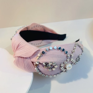 Detail eines rosa gefalteten Stirnbands mit silbernen Metallnieten und großer Perle