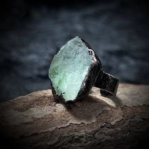Macro detail of natural green raw stone ring with vintage hammered metal band on wood