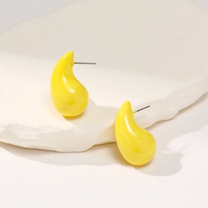 Macro view of bright yellow teardrop stud earrings on a textured white stone base