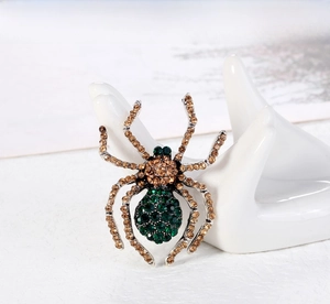 Close-up of vintage spider brooch with green and amber rhinestones on a ceramic stand