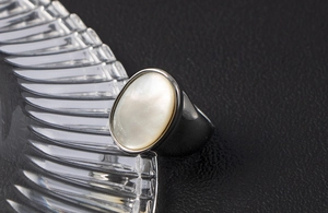 Macro di un anello minimalista con intarsio in conchiglia bianca su metallo grigio scuro