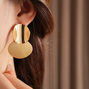 Close-up of golden oval brushed metal earrings on a model with warm natural lighting